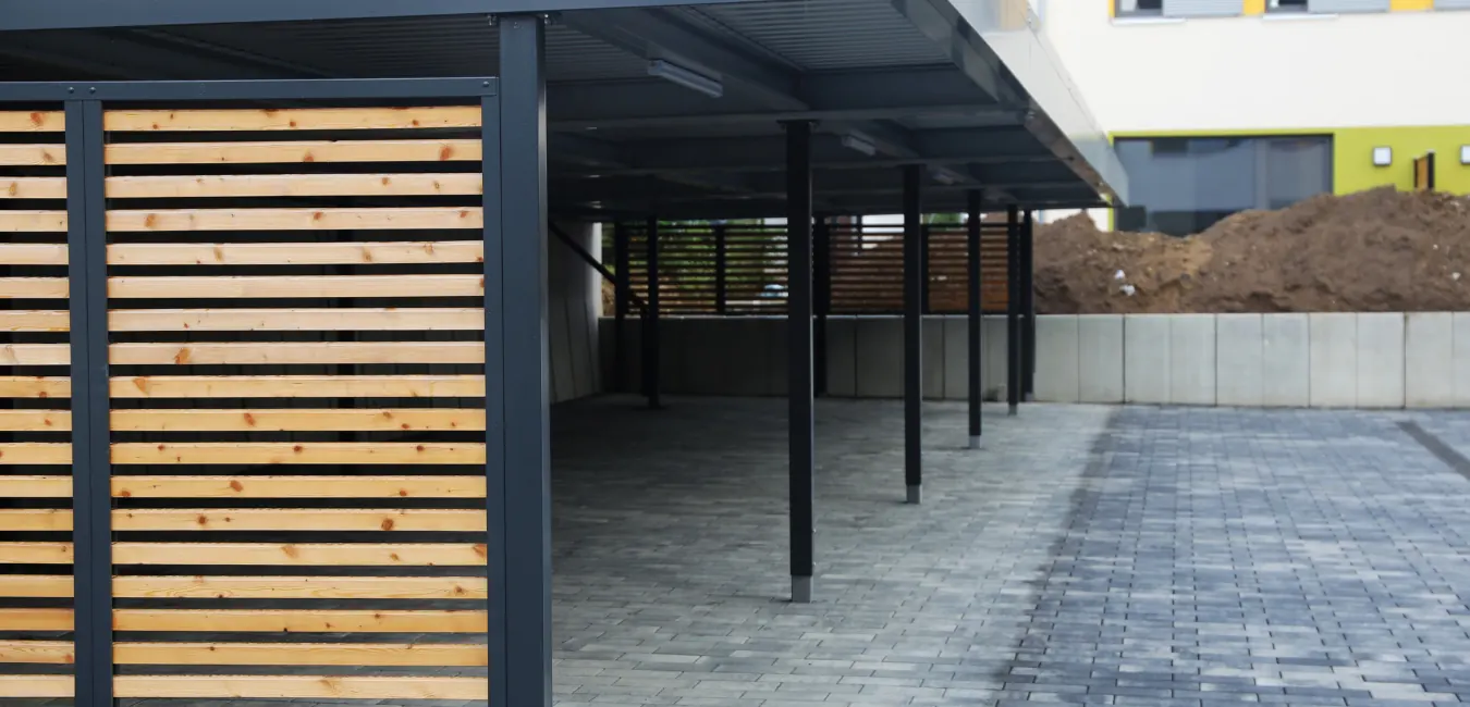 Multi-bay steel carport with dark posts and slatted timber screen